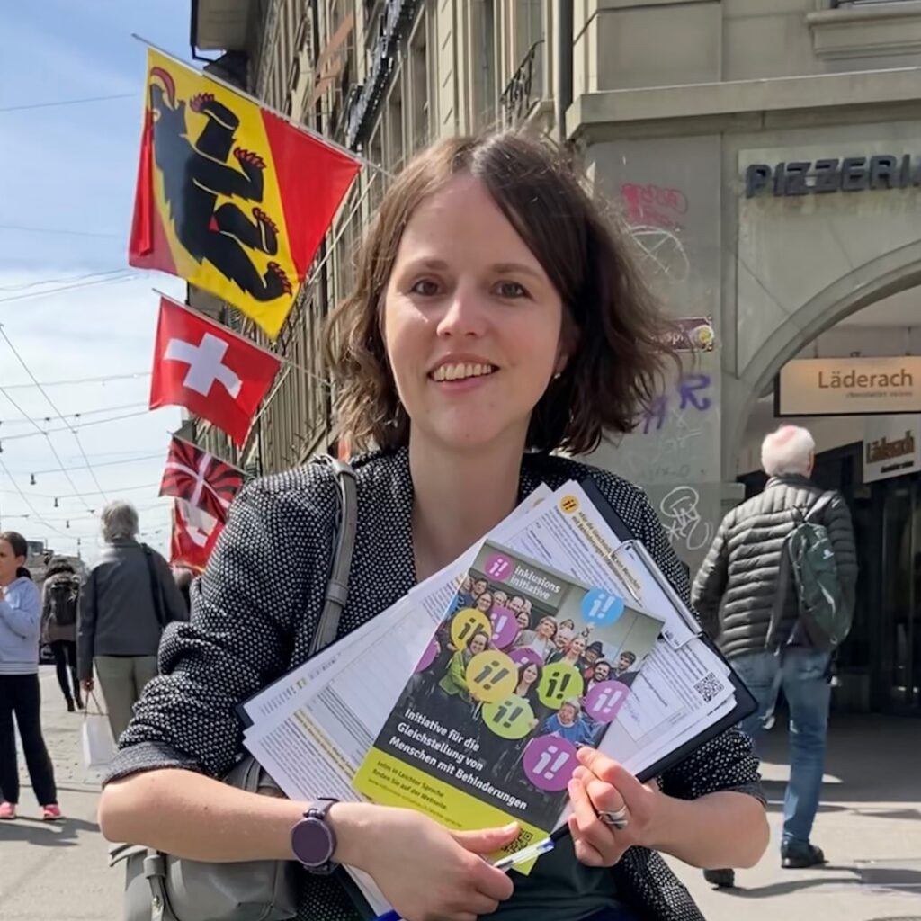 Portrait von Sina Eggimann in Bern. Sina hält Unterschriftenbögen und die Broschüre der Inklusions-Initiative in der Hand. 
